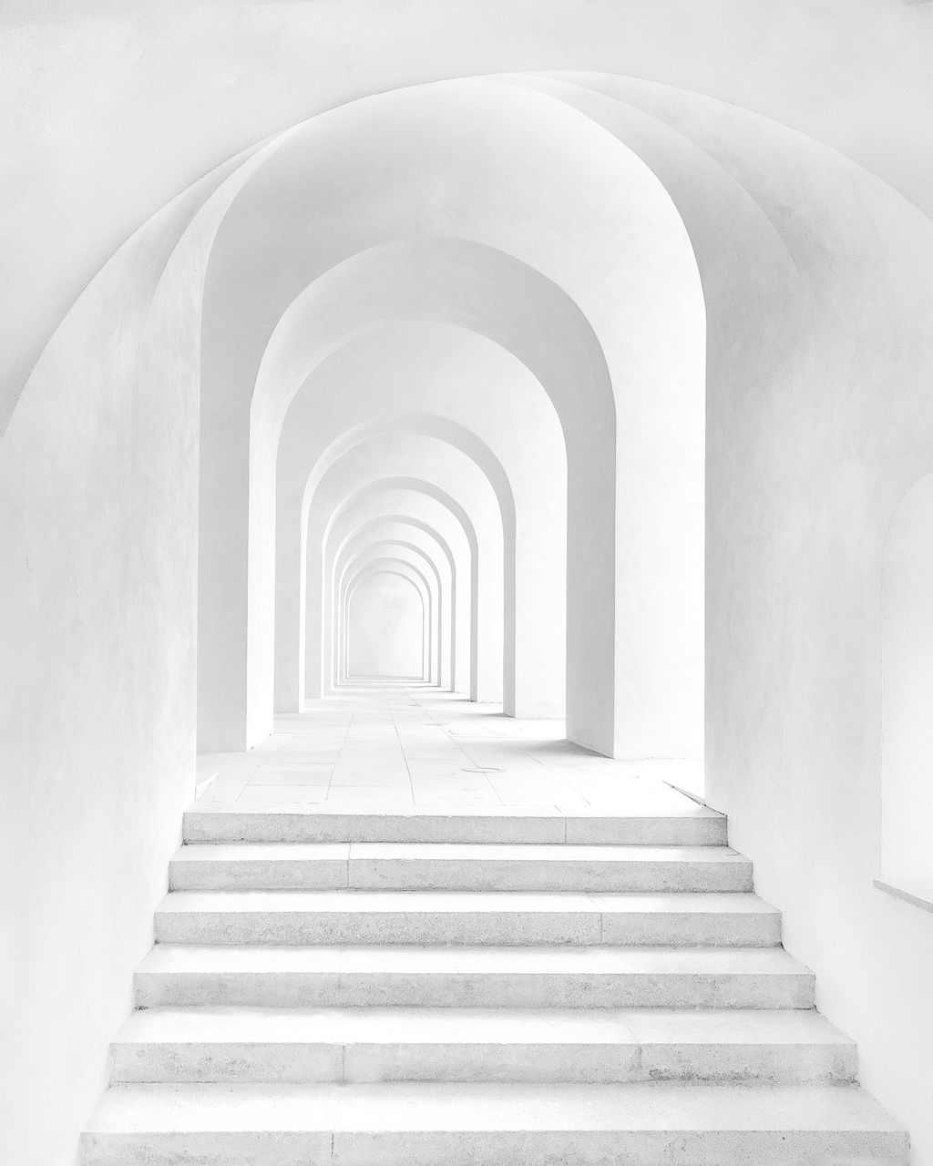 White arches and stone steps leading forward into soft light