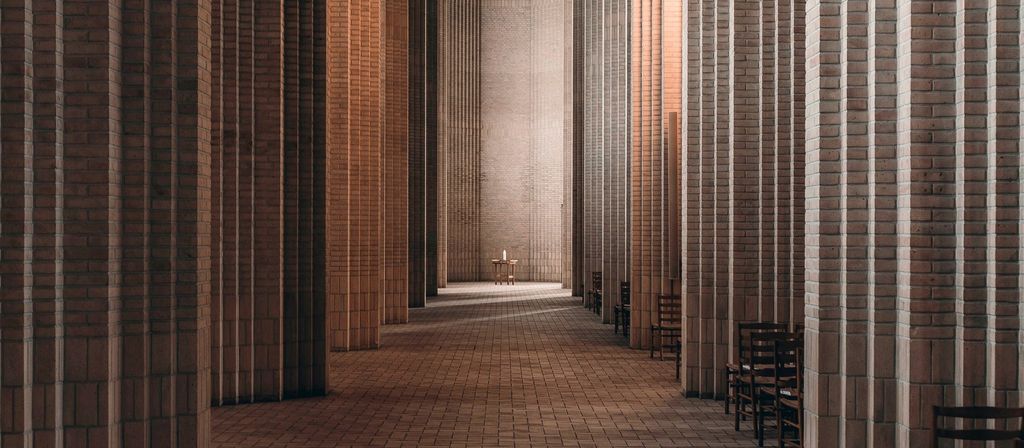 A long colonnade of brick columns and arches, receding toward a lit doorway
