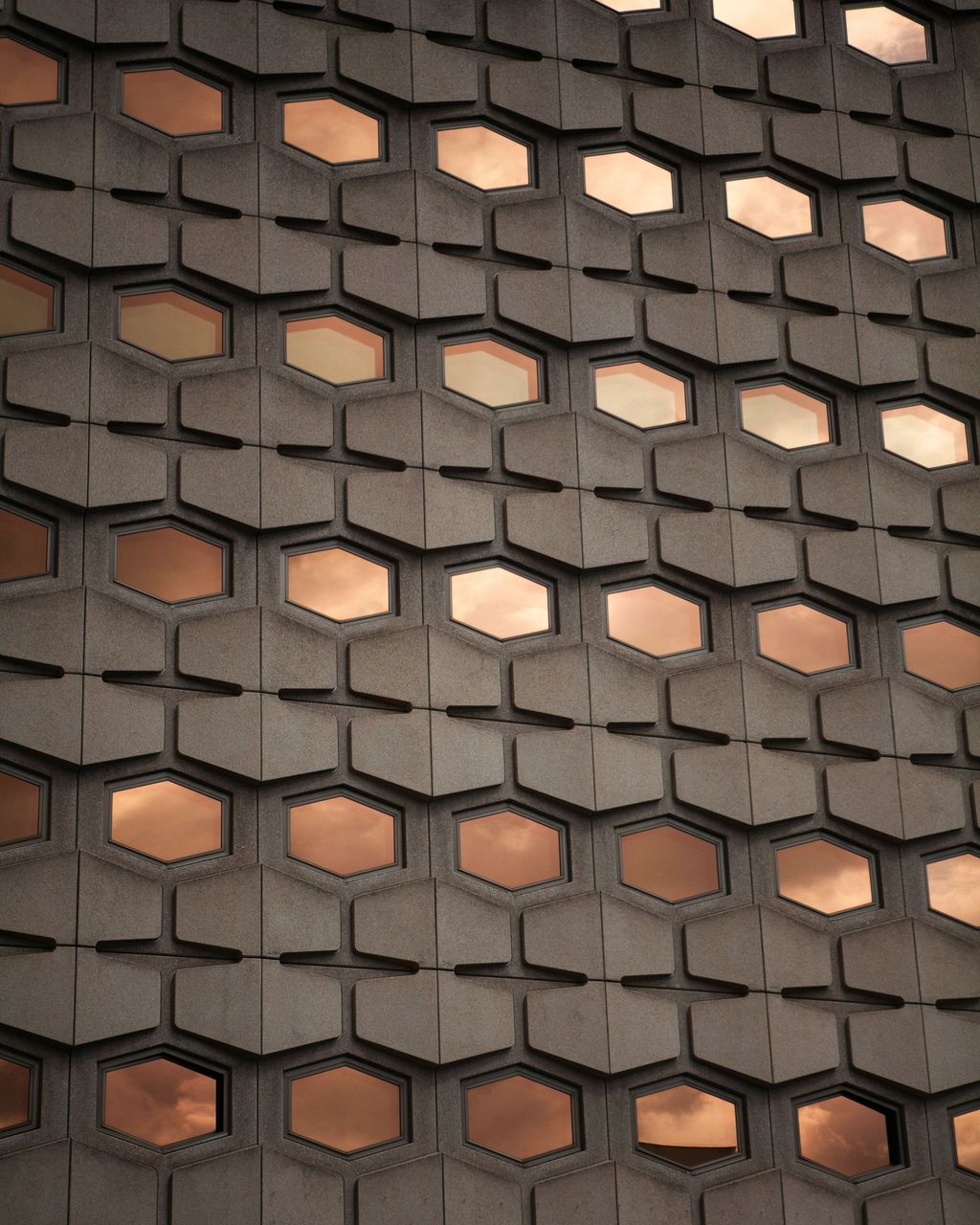 A stone facade of hexagonal windows, lit warm from within at dusk