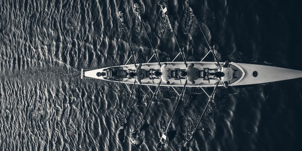 A rowing crew seen from above, moving in unison across dark water